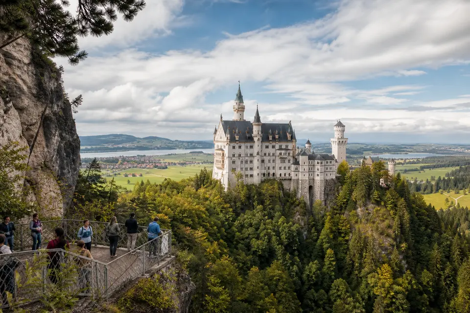 AI-generated illustration of travellers viewing Neuschwanstein Castle in a wooded landscape